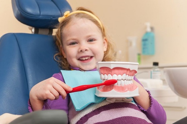 A girl with a red toothbrush brushing the dental prosthteic