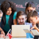 A teacher with a laptop, surrounded by a group of students who are learning something on the laptop as per the instructions of a teacher.