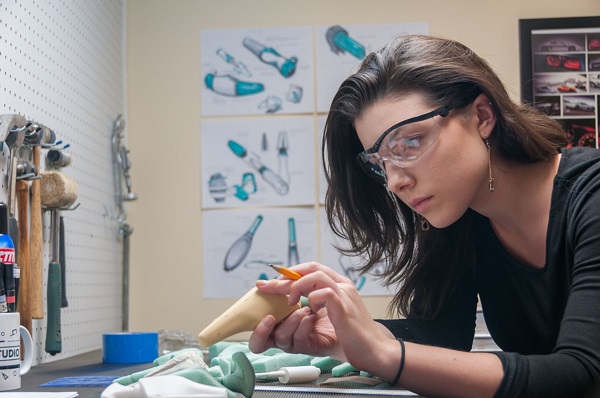 A girl has worn specs and is having a pencil on her hand and checking a model of a product which she had created before.